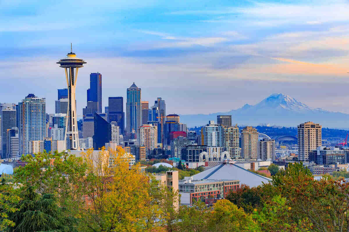 Seattle skyline with Space Needle in the foreground, modern buildings, and Mount Rainier in the background under a partly cloudy sky.